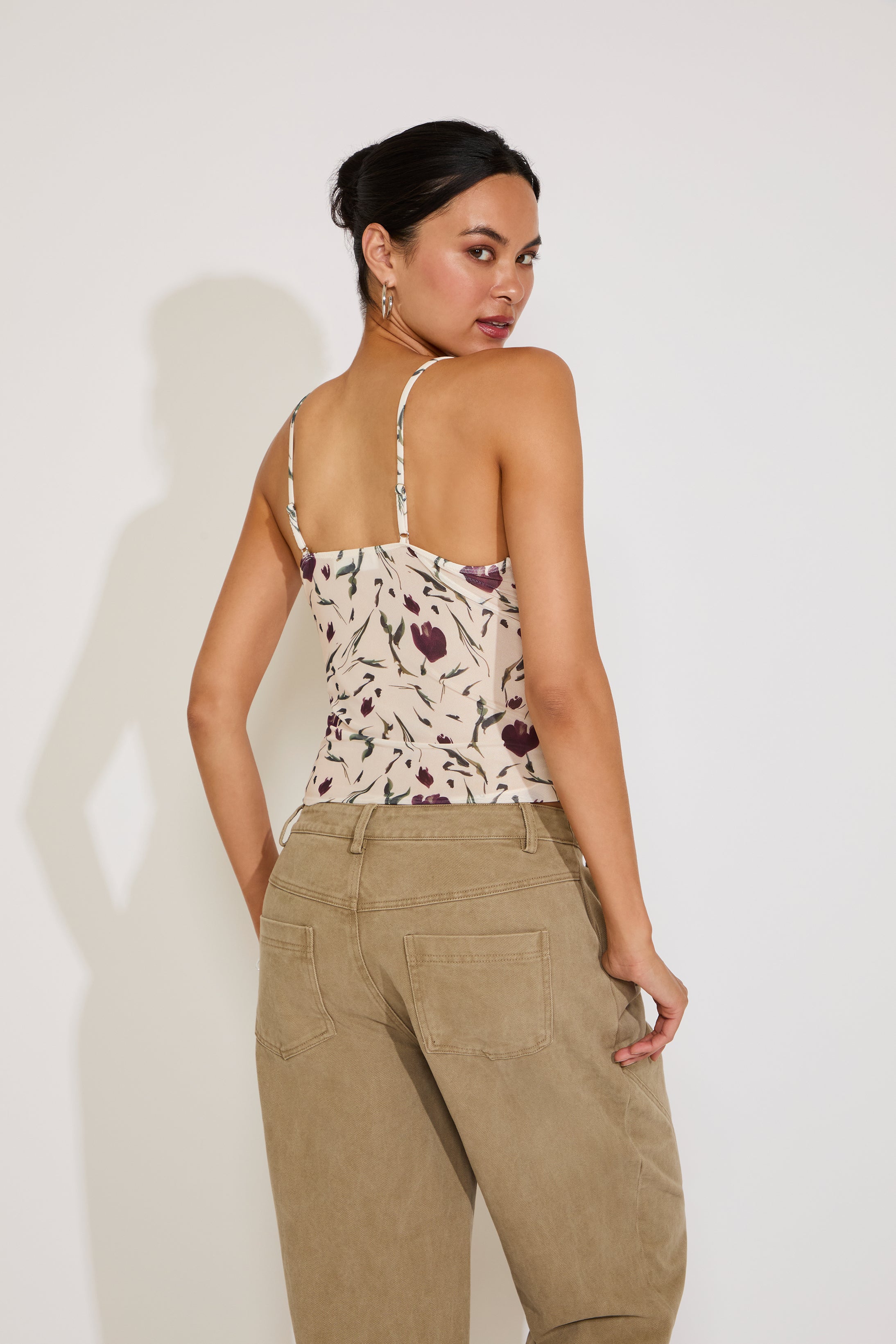 Woman wearing a floral top and beige pants against a white background