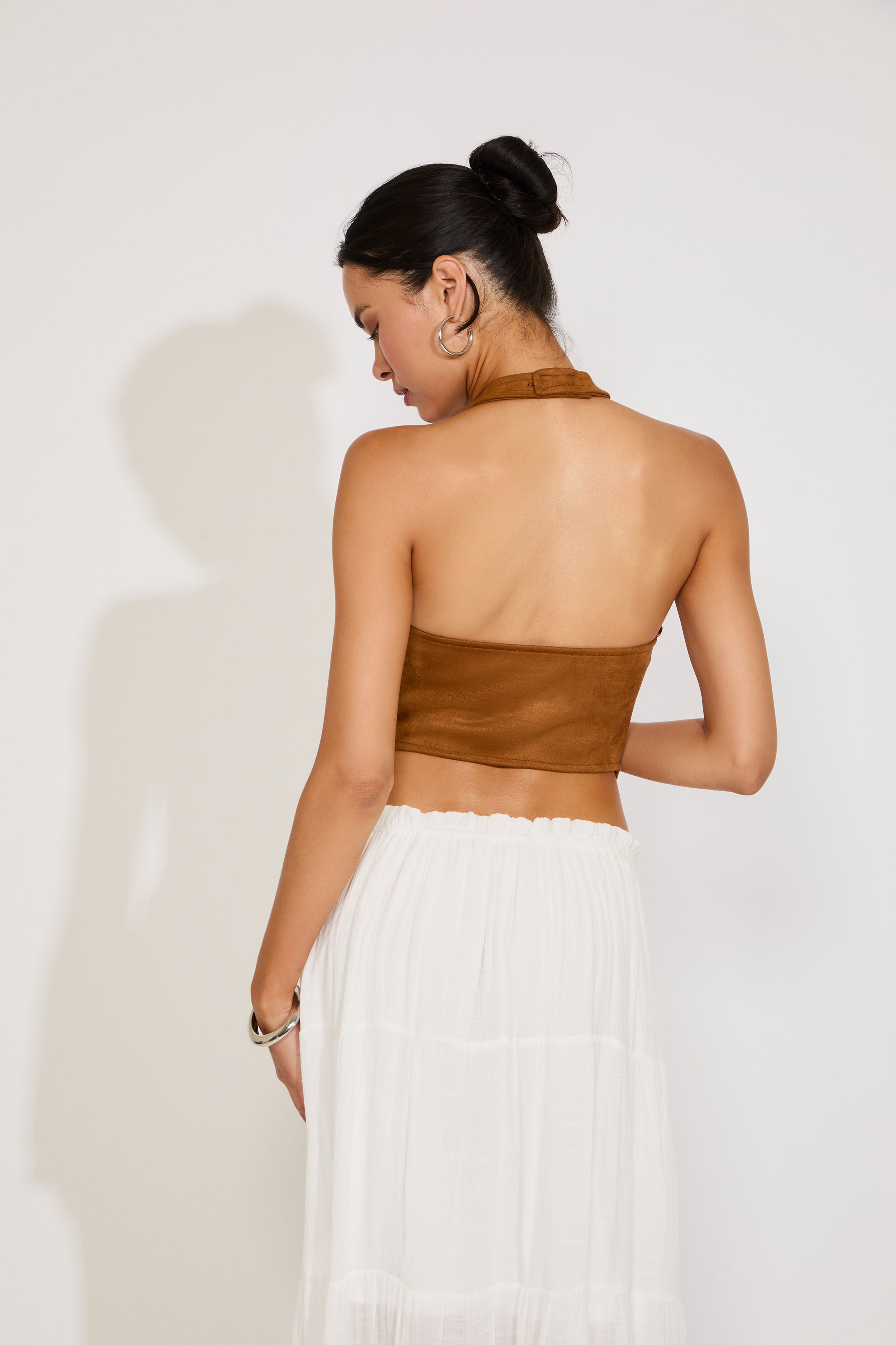 Woman wearing a brown halter top and white skirt against a white background