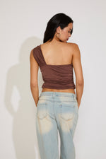 Woman wearing a brown one-shoulder top and light blue jeans against a white background