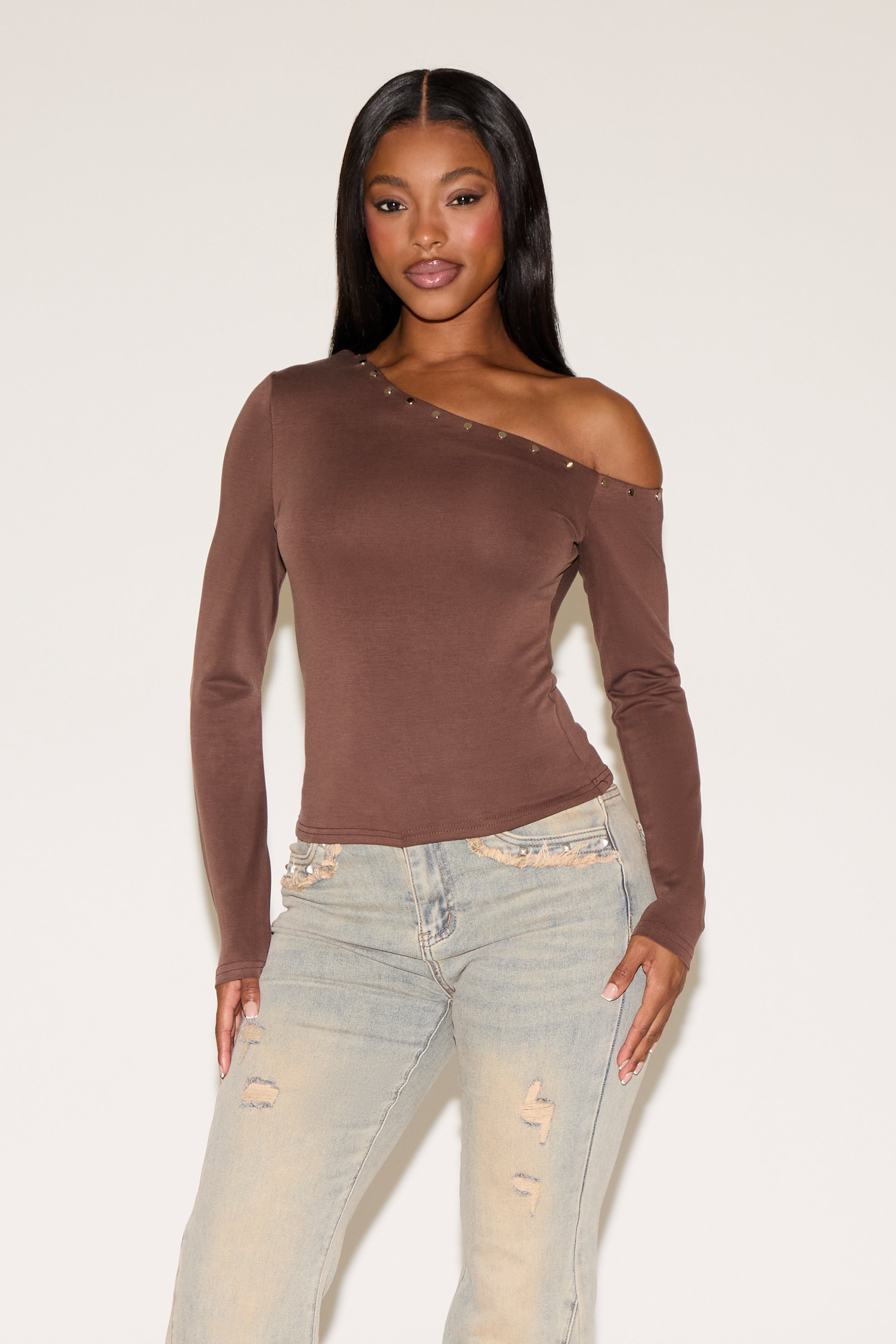Woman wearing a brown one-shoulder top and light blue jeans on a white background