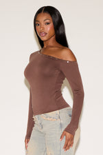 Woman wearing a brown off-shoulder top with light blue jeans on a white background