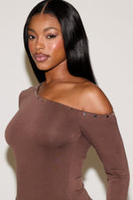 Woman wearing a brown off-shoulder top with decorative elements on a plain background