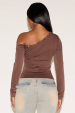 Woman wearing a brown one-shoulder top with studded details on a plain background