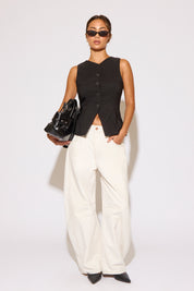 Woman wearing a black sleeveless top and white pants against a white background