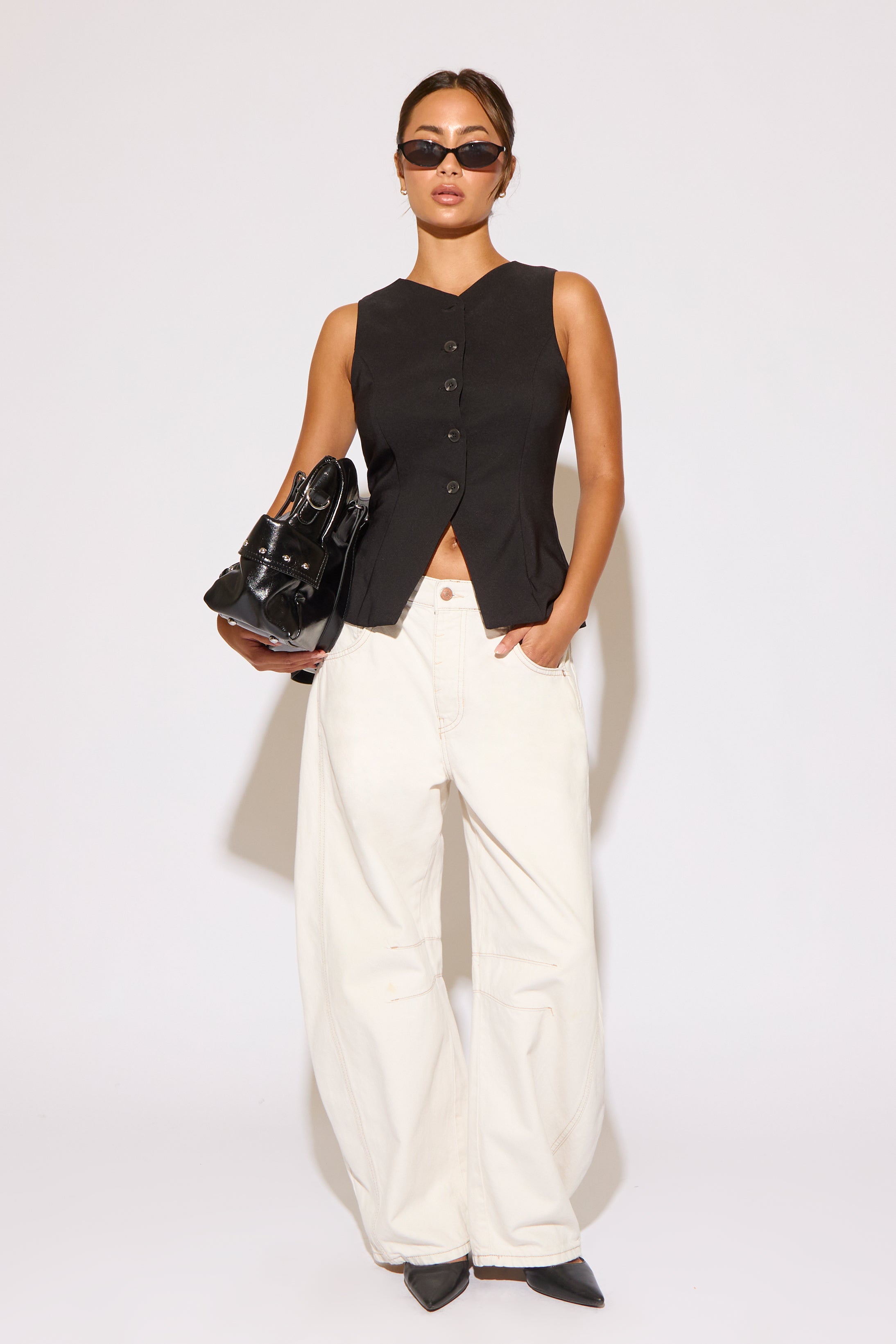 Woman wearing a black sleeveless top and white pants against a white background