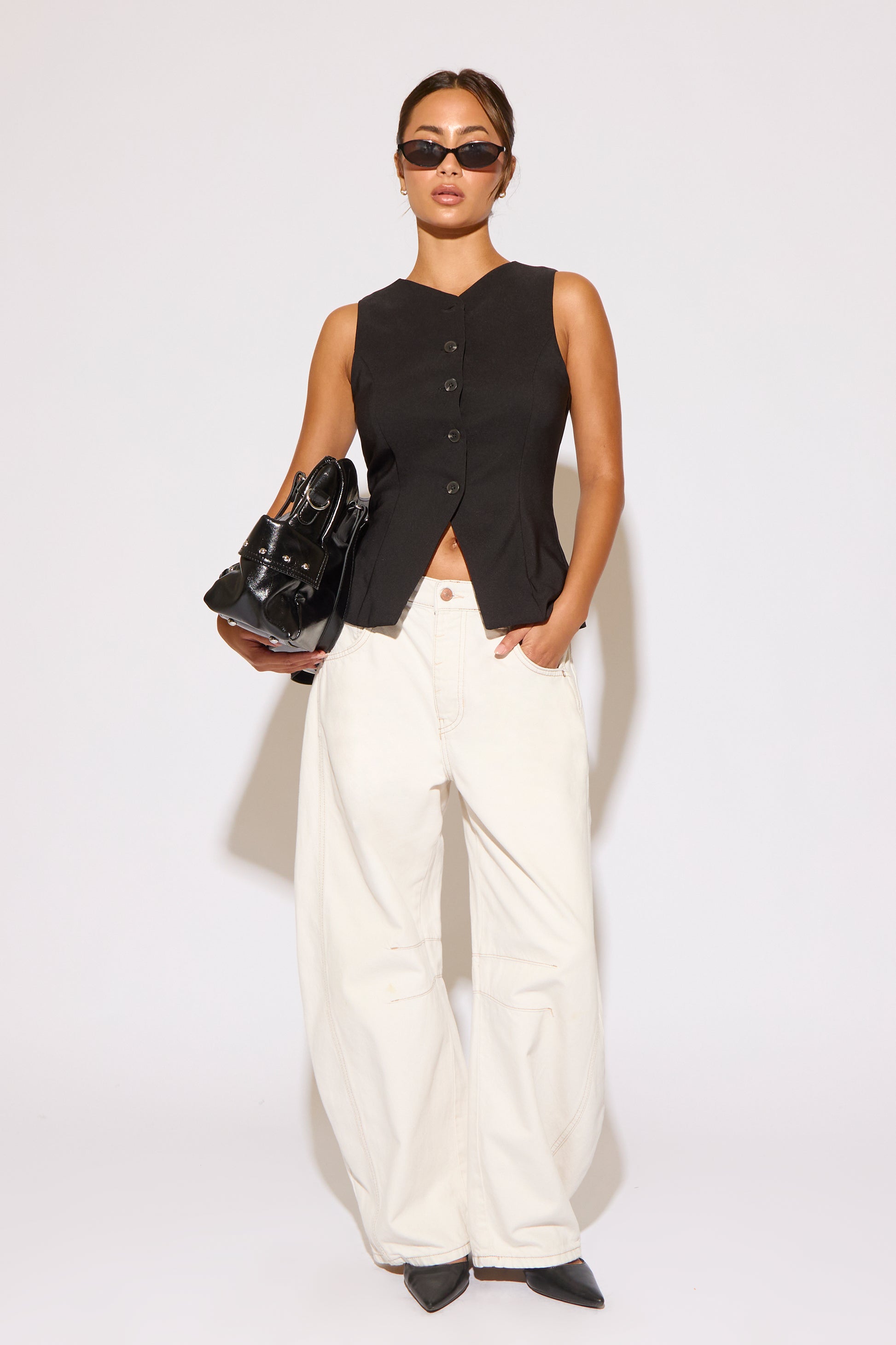 Woman wearing a black sleeveless top and white pants against a white background