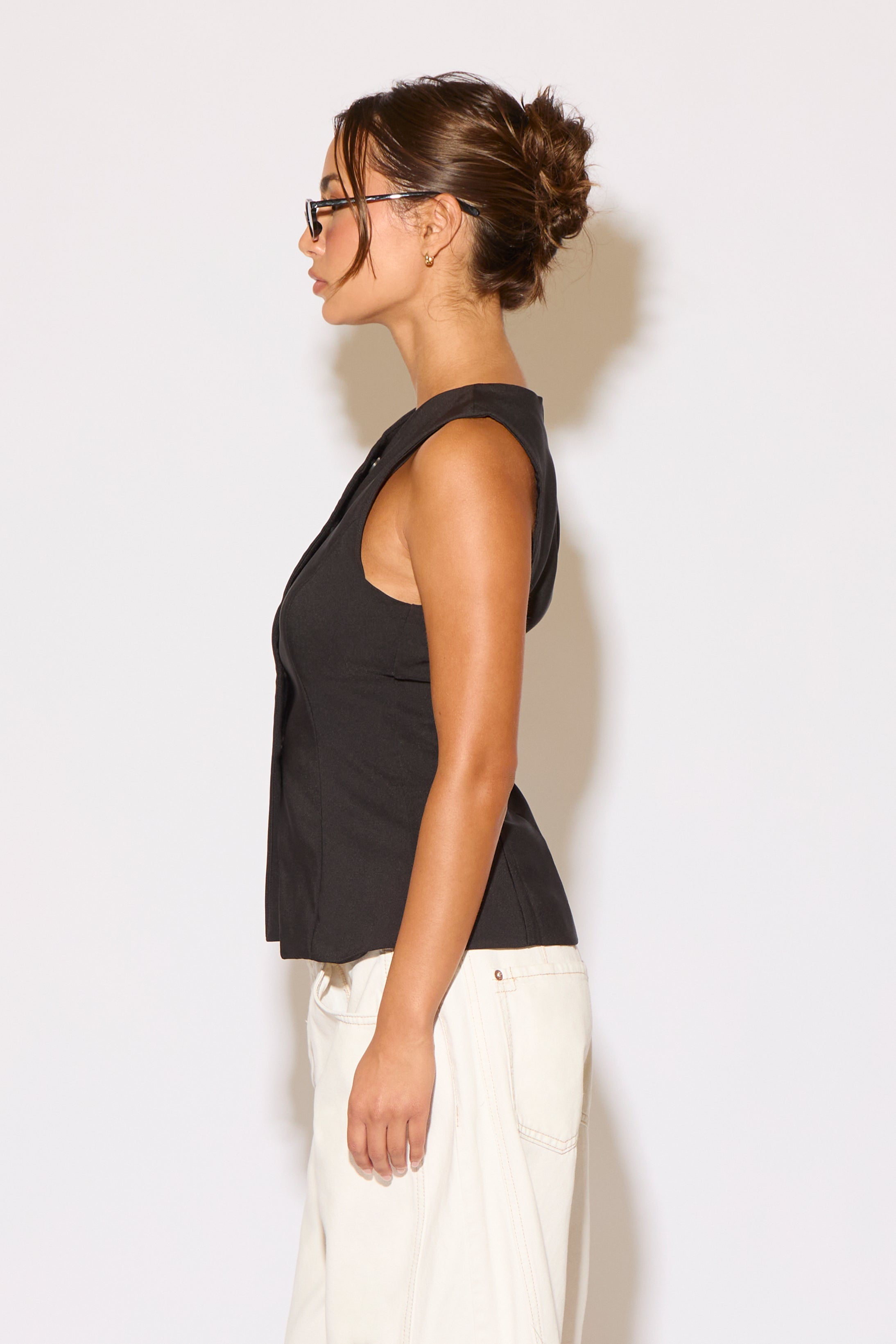 Woman wearing a black sleeveless top and white pants against a plain background