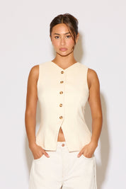 Woman wearing a cream top and white pants on a white background