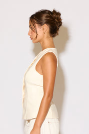 Woman wearing a cream top and white pants on a white background