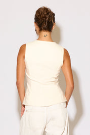 Woman wearing a cream top and white pants on a white background
