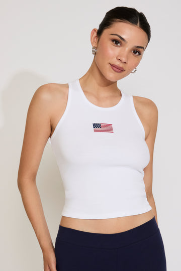 Woman wearing a white tank top with an American flag emblem on a plain background