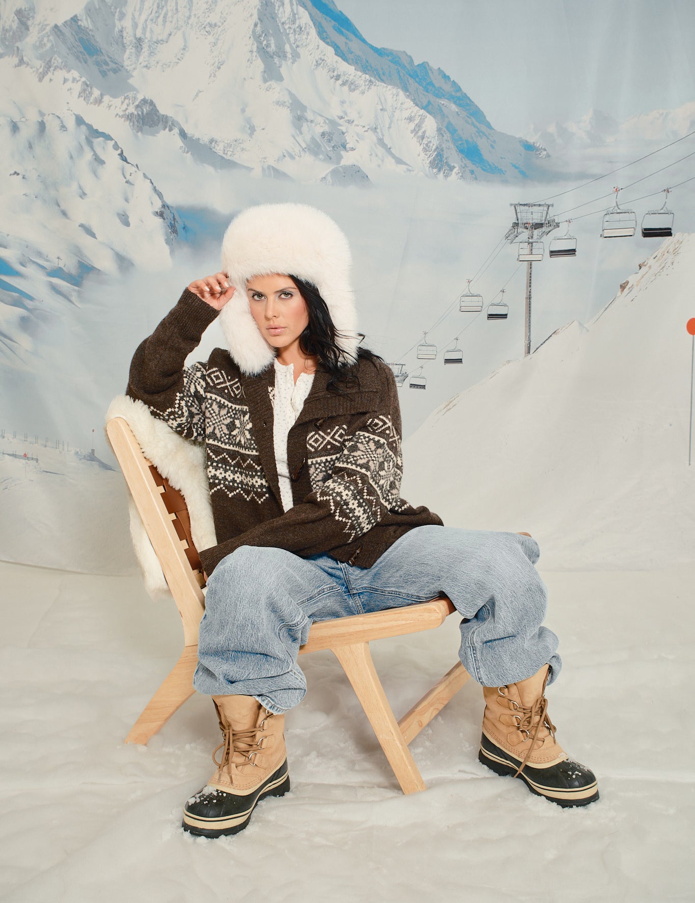 Person sitting on a wooden stool in a snowy landscape with mountains in the background