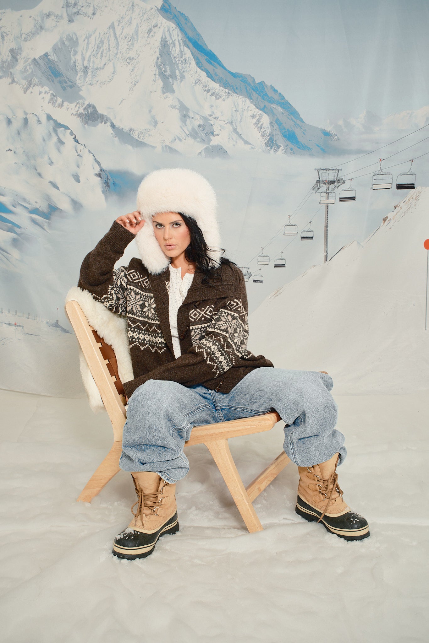 Person sitting on a wooden stool in a snowy landscape with mountains in the background