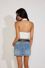 Woman wearing a white strapless top and denim skirt against a plain background