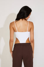 Woman wearing a white tank top and brown pants against a plain background