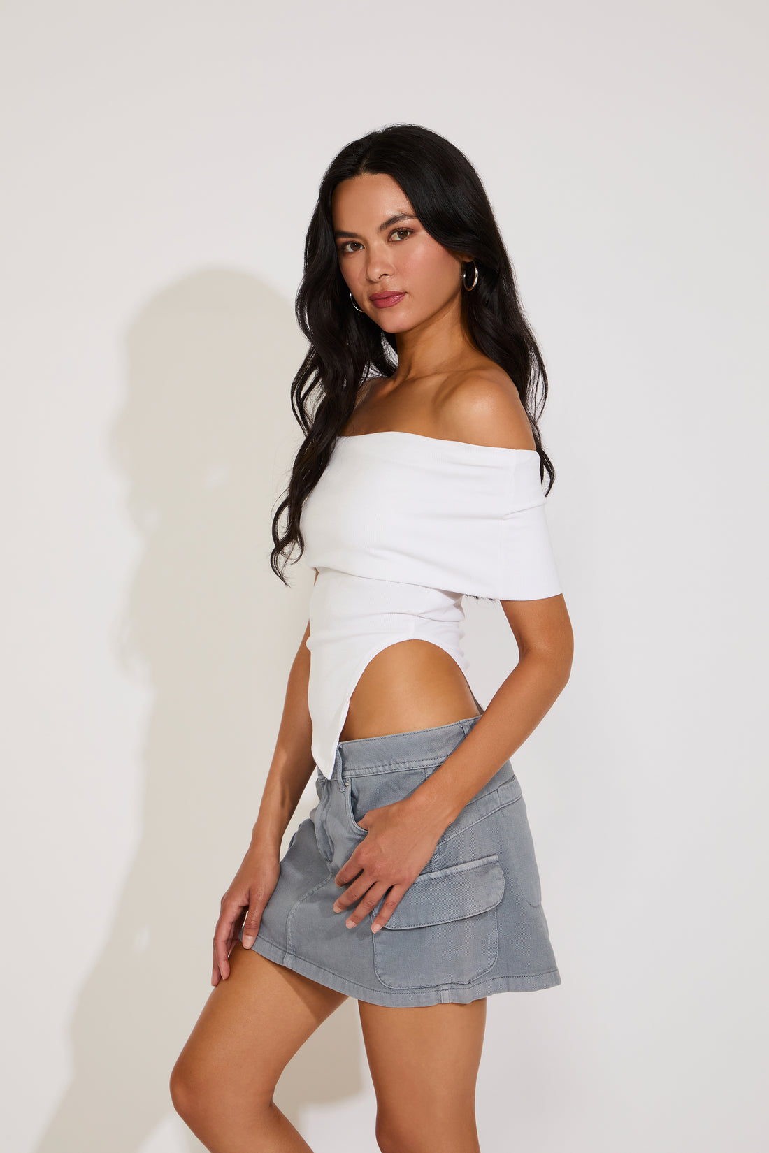 Woman wearing a white off-shoulder top and gray pants on a plain background