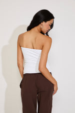 Woman wearing a white strapless top and brown pants against a plain background