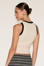 Woman wearing a beige sleeveless top with black accents against a plain background