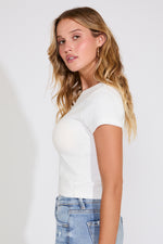 Woman wearing a white t-shirt and blue jeans against a plain background