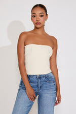 Woman wearing a white strapless top and blue jeans against a plain background