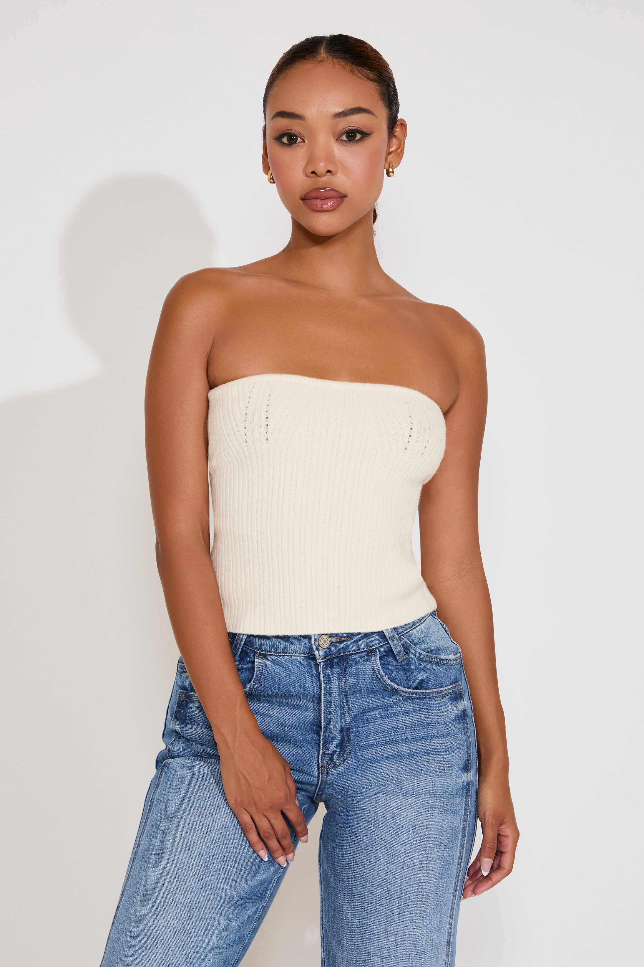 Woman wearing a white strapless top and blue jeans against a plain background