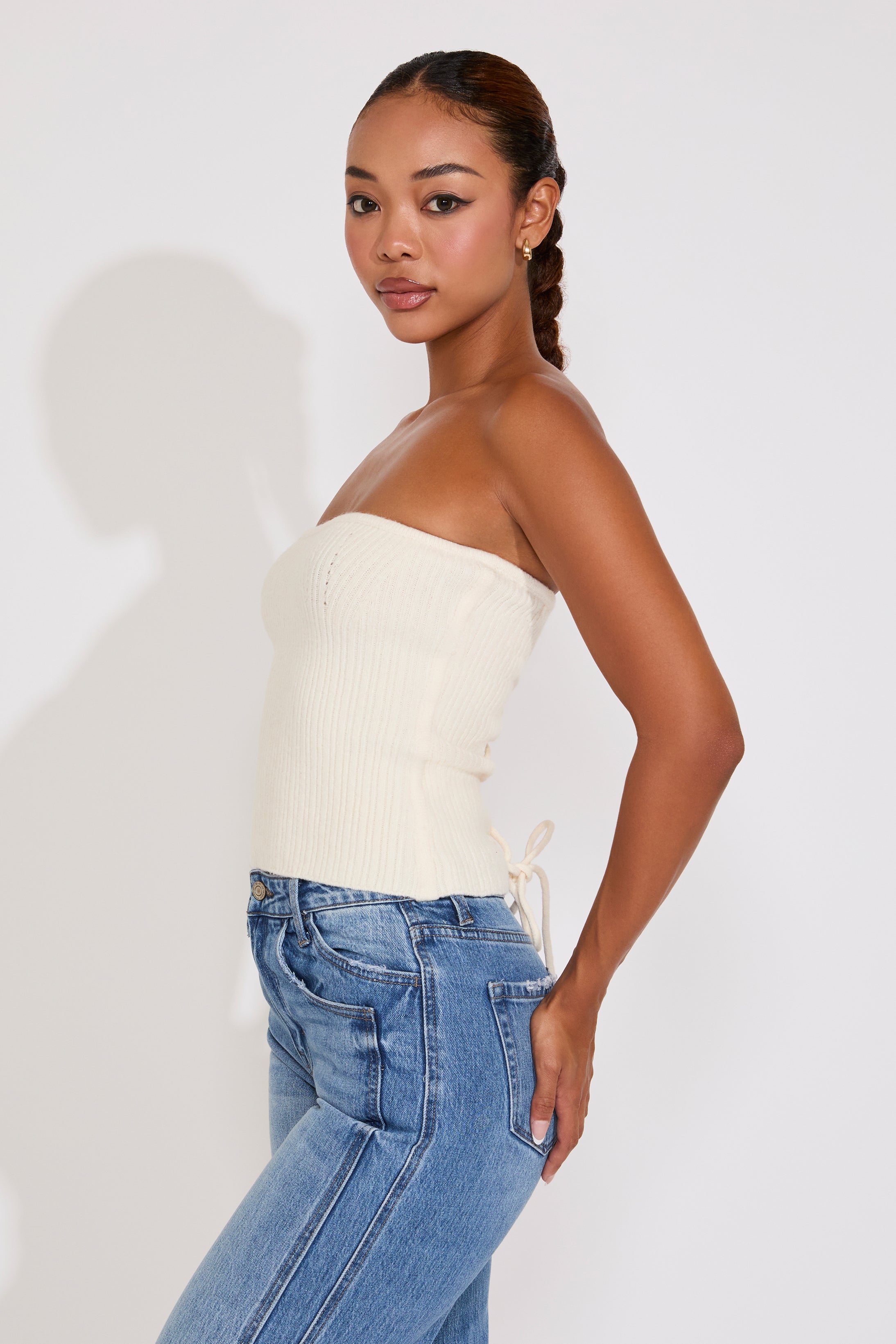 Woman wearing a white strapless top and blue jeans on a plain background