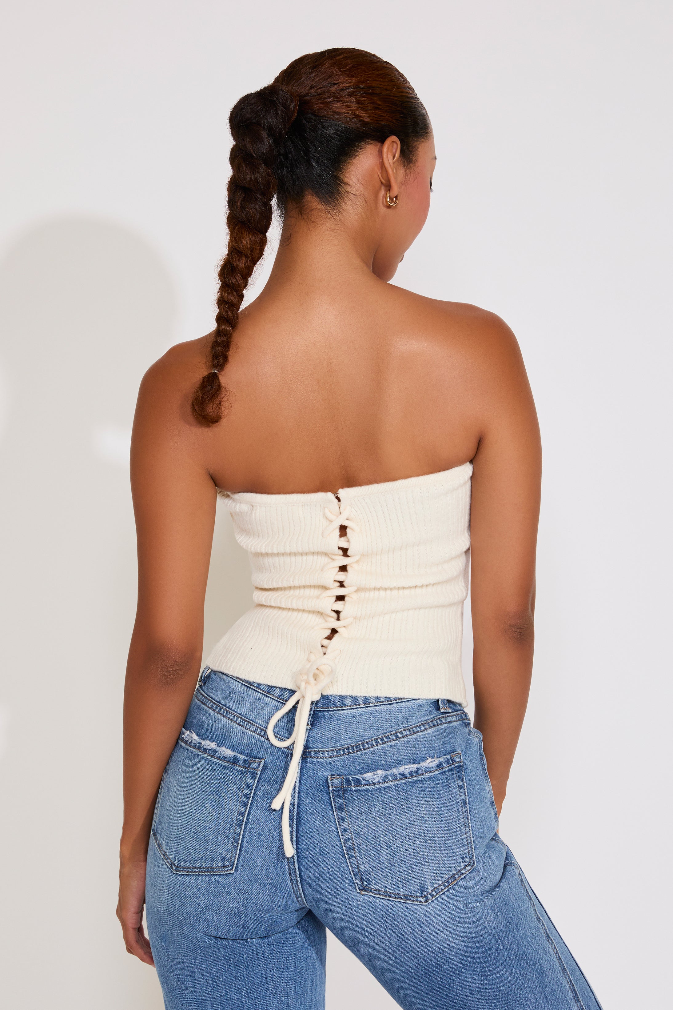 Woman wearing a white strapless top and blue jeans against a plain background