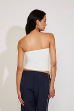 Woman wearing a white strapless top and navy pants against a plain background