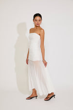 Woman wearing a strapless white dress with sheer overlay on a plain background