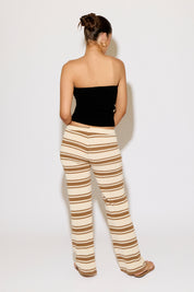 Woman wearing a black strapless top and beige and brown striped pants on a white background