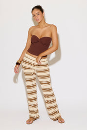 Woman wearing a brown strapless top and striped pants on a white background