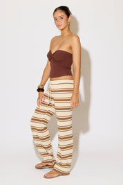 Woman wearing a brown strapless top and striped pants on a white background