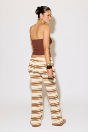 Woman wearing a strapless brown top and striped pants on a white background