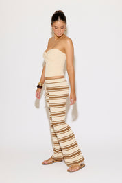 Woman wearing a beige strapless top and striped pants on a white background