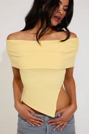 Woman wearing a yellow off-shoulder top against a plain background