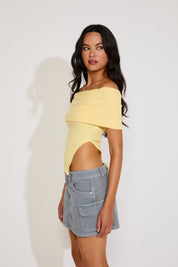 Woman wearing a yellow off-shoulder top and denim skirt on a white background