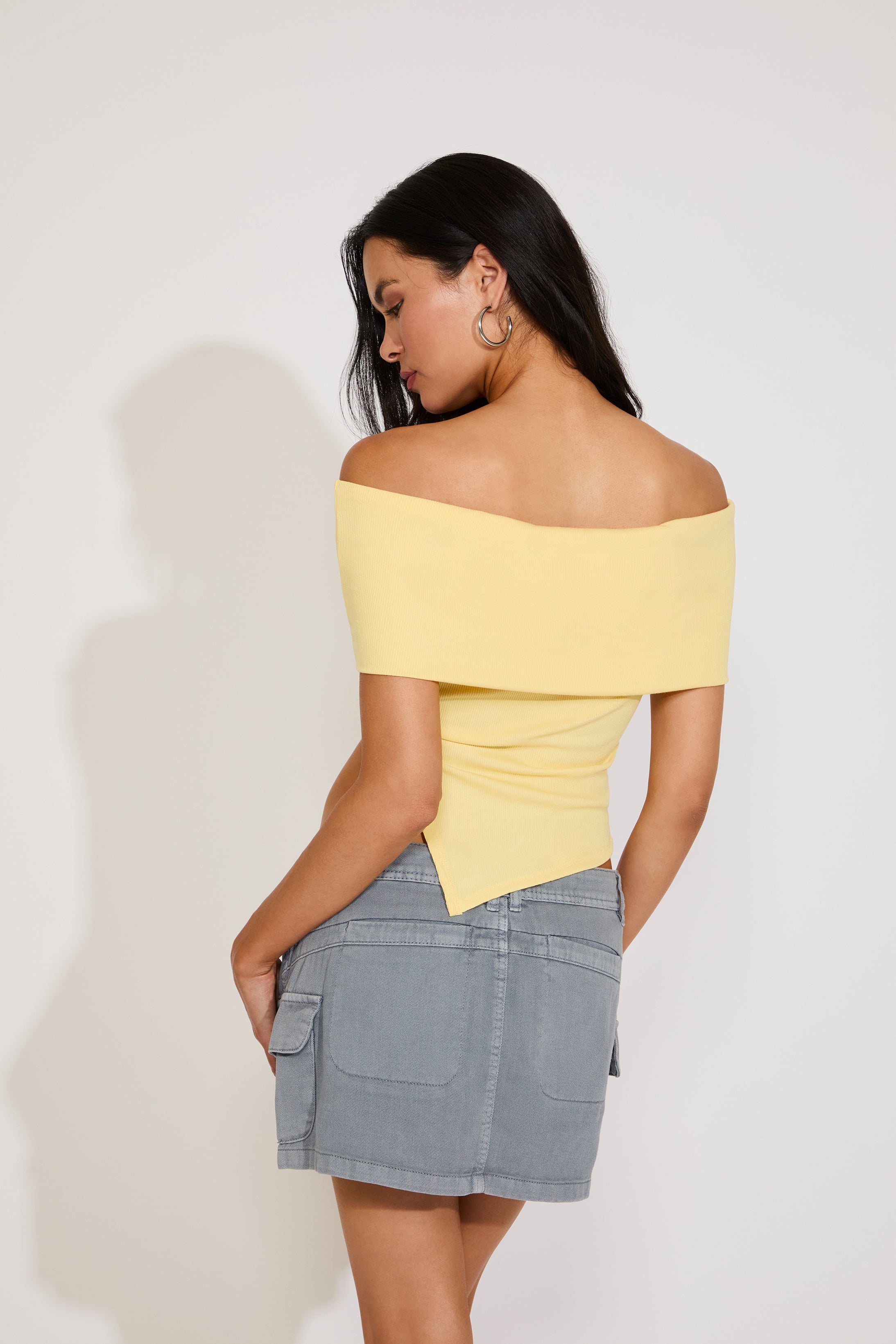 Woman wearing a yellow off-shoulder top and gray skirt against a white background
