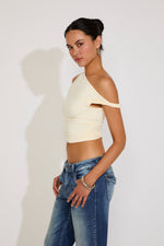 Woman wearing a beige crop top and blue jeans against a plain background