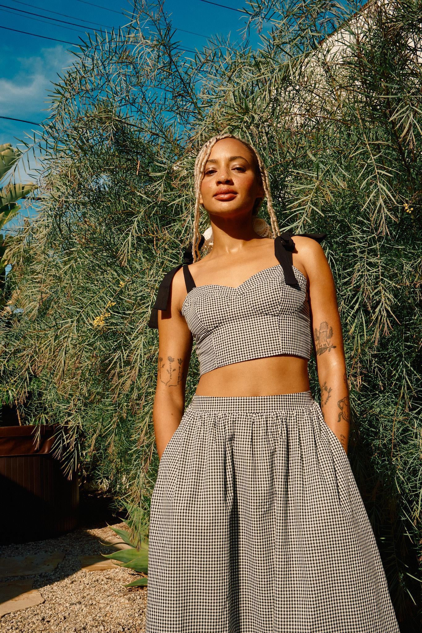 A person wearing a high rise black and white checkered maxi skirt with a crop top and white sneakers standing outdoors.