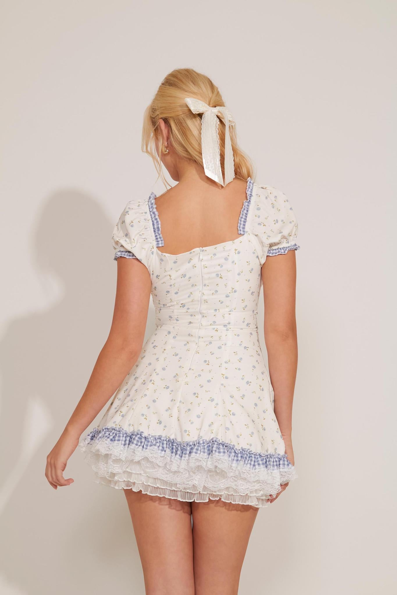 A sleeveless white dress with floral print and blue gingham trim, featuring a square neckline and ruffled details.