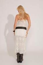 A person wearing a white maxi skirt with a rose pattern and lace detailing, with a white backgrounde background.