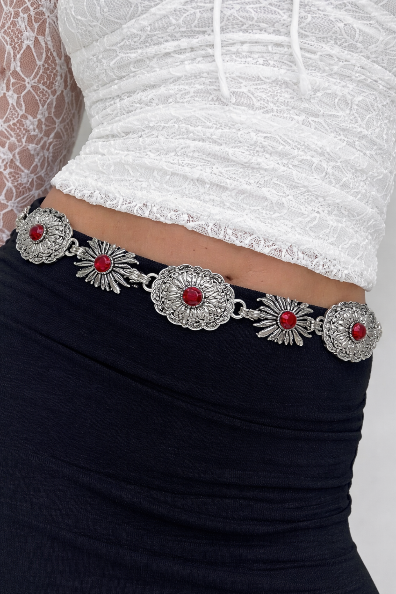 Decorative belt with red stones and silver patterns worn by a person in a white top and black pants.
